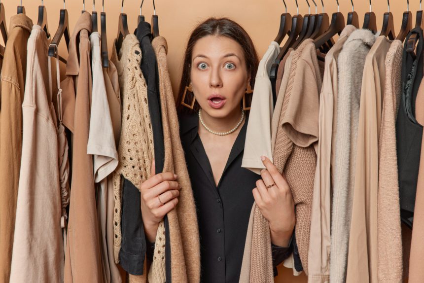 Surprised dark haired young European woman stares impressed her presence near rack signifies fusion